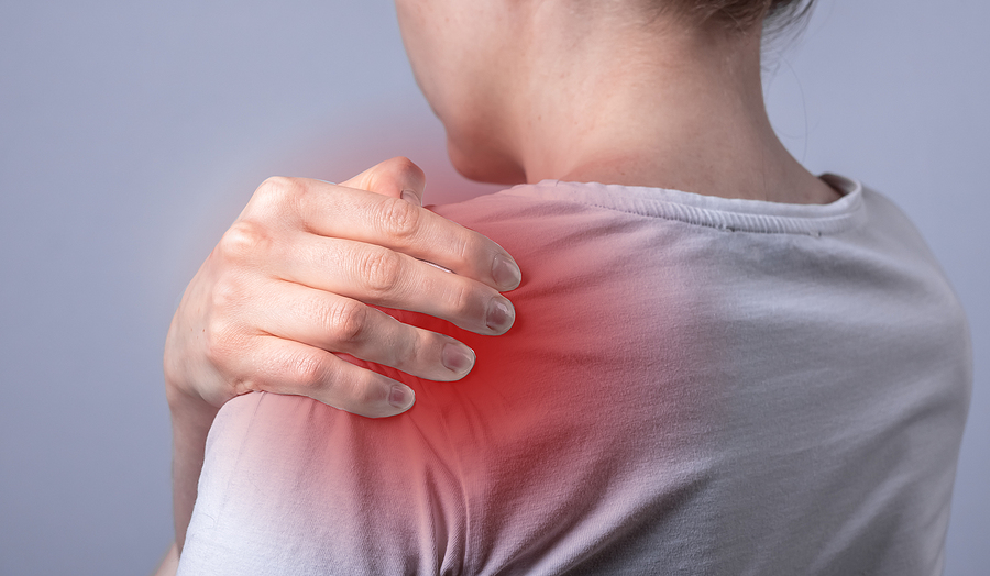 Person experiencing shoulder pain, holding shoulder with hand, highlighting discomfort or injury.