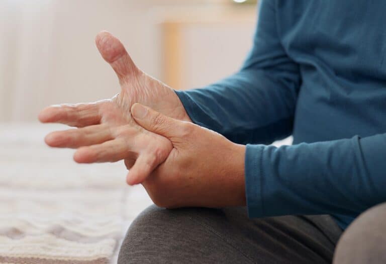 Person experiencing wrist pain, holding their hand with the other hand, in a clinical setting.